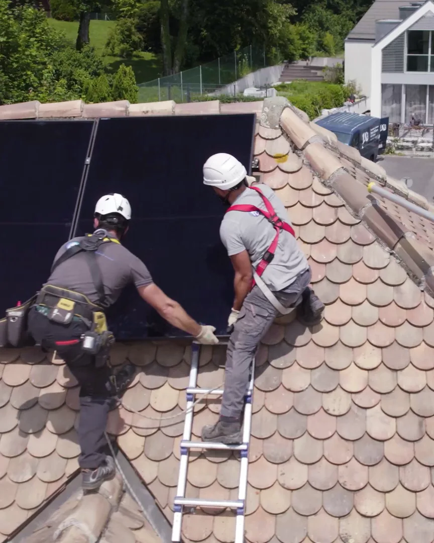 Deux techniciens Home Intelligence posent un panneau solaire sur une toiture en tuiles