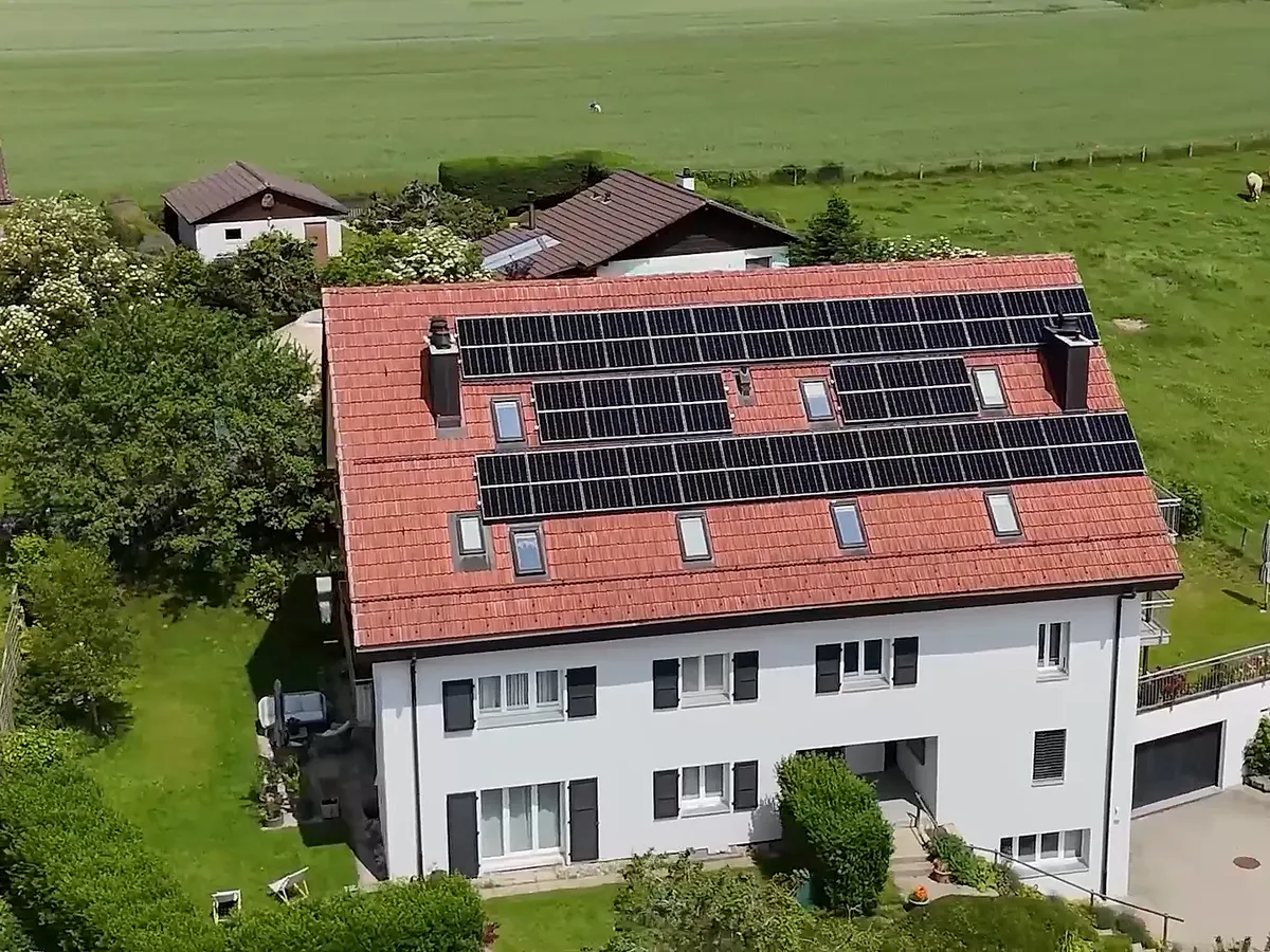 Maison à toit de tuiles rouges équipée de panneaux solaires, vue aérienne, prairie en bordure