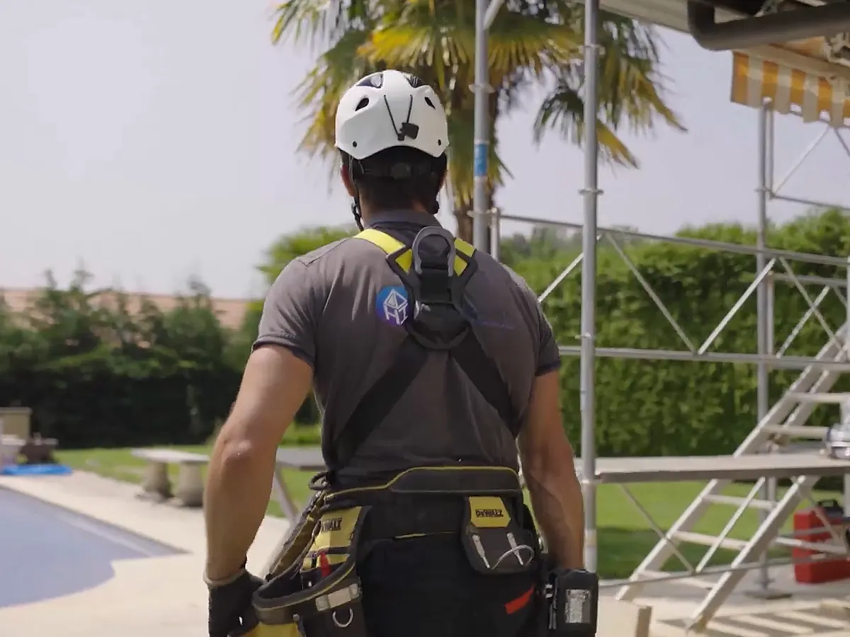 Technicien harnaché, casque et ceinture à outils, devant un échafaudage