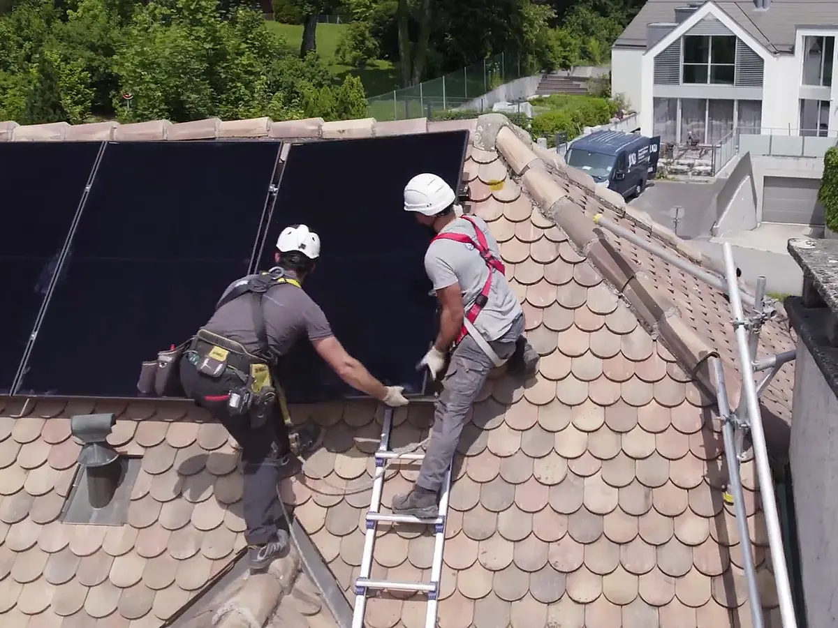 Deux techniciens manipulant un module solaire sur une toiture en tuiles