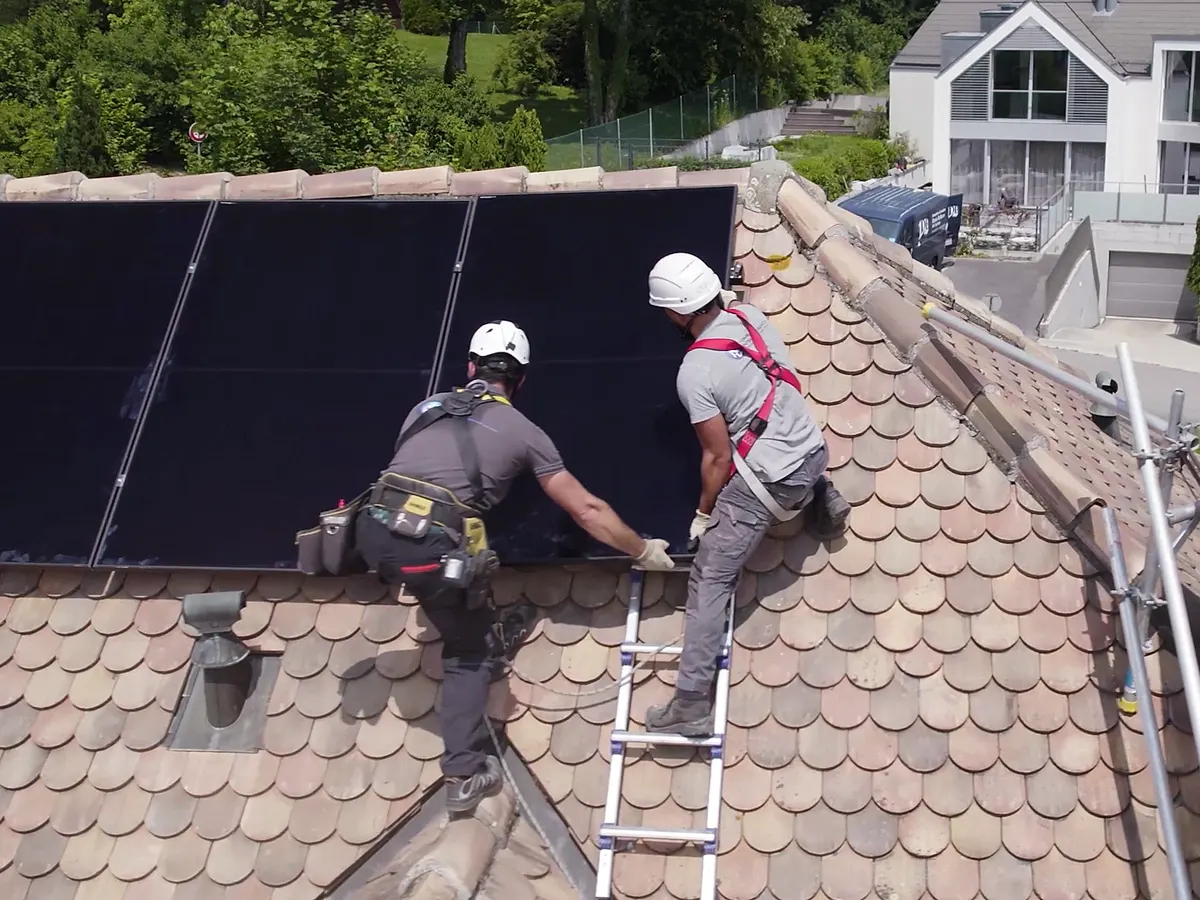 Deux techniciens posant un module solaire sur une toiture en tuiles