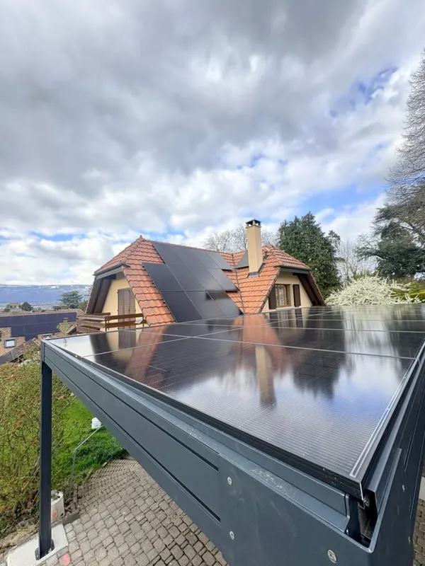 Toiture à pans multiples avec panneaux noirs, carport solaire au premier plan, vue sur le lac.