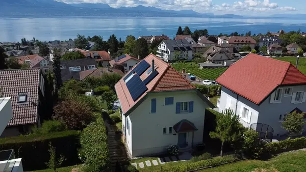 Villa au toit de tuiles avec panneaux solaires, village en pente au bord d'un grand lac.