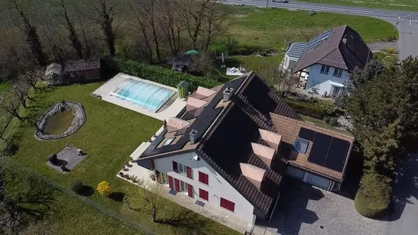 Grande bâtisse de type ferme avec panneaux solaires, piscine couverte et étang paysager.