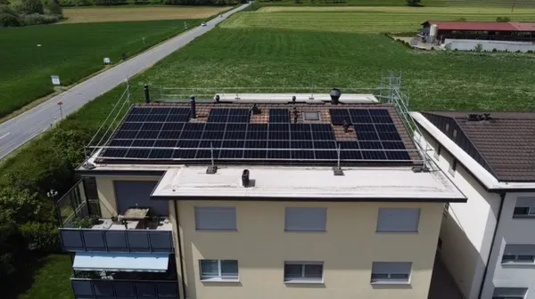 Immeuble à toit plat couvert de panneaux solaires, champs plats et ferme voisine.