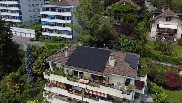 Immeuble résidentiel entouré de verdure luxuriante, toiture à tuiles couverte de panneaux.