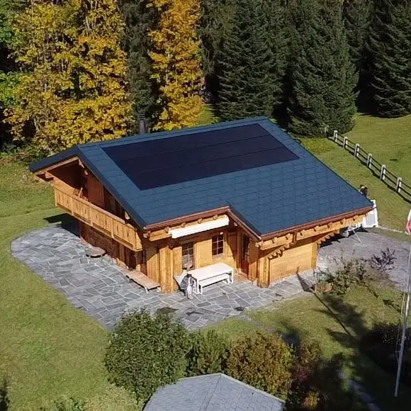 Chalet en bois traditionnel entouré de conifères, toit couvert de panneaux solaires sombres.