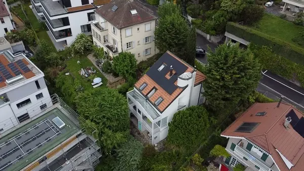 Villa à tourelle avec panneaux solaires en toiture, immeubles et jardins denses alentour.