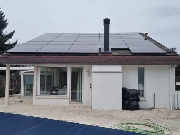 Façade basse d'une villa avec toiture couverte de panneaux, piscine bâchée au premier plan.
