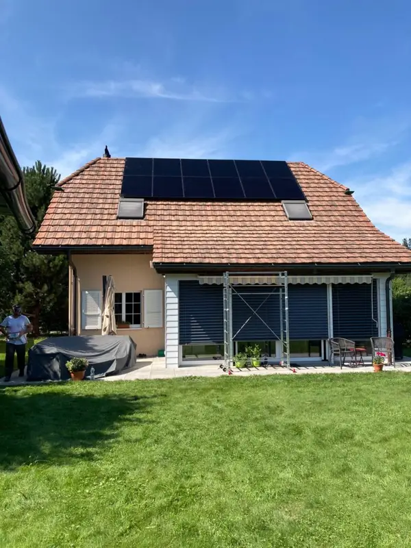 Maison traditionnelle aux volets blancs, toiture couverte de panneaux, jardin engazonné et technicien présent.