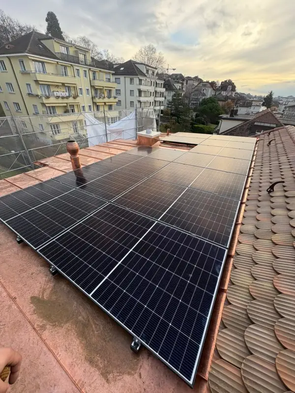 Vue depuis une toiture plate avec panneaux, immeubles citadins denses et grue de chantier au loin.