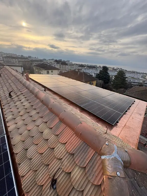 Panneaux solaires posés sur une toiture à tuiles, panorama urbain dense sous un ciel couchant.