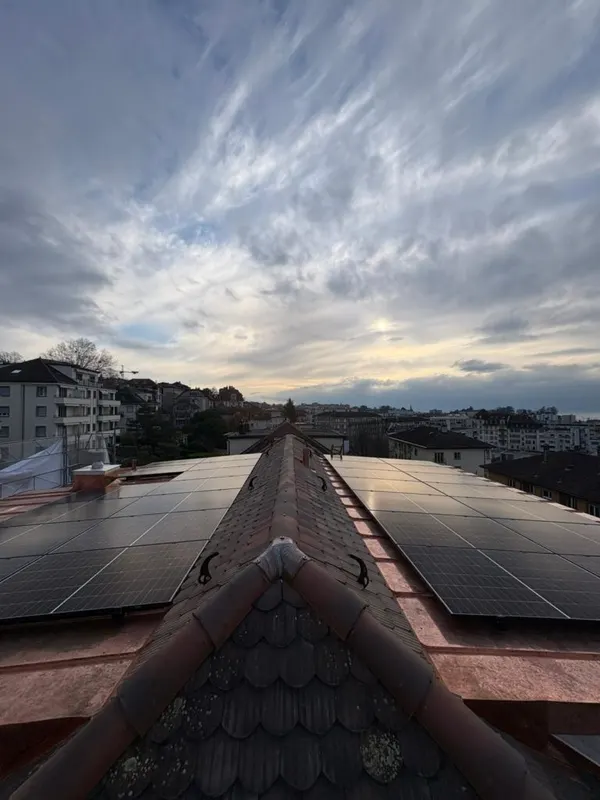 Faîtage de toiture avec panneaux des deux côtés, skyline urbaine dense sous un ciel nuageux.