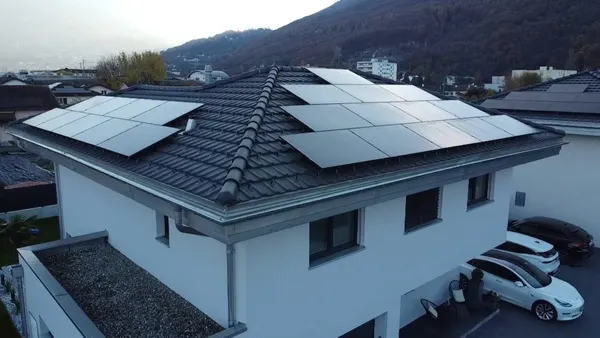 Toiture d'une villa couverte de panneaux, montagne boisée escarpée et ville en arrière-plan.