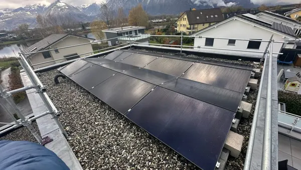 Toiture plate avec panneaux solaires sur lestage de gravier, sommets enneigés et plaine agricole.